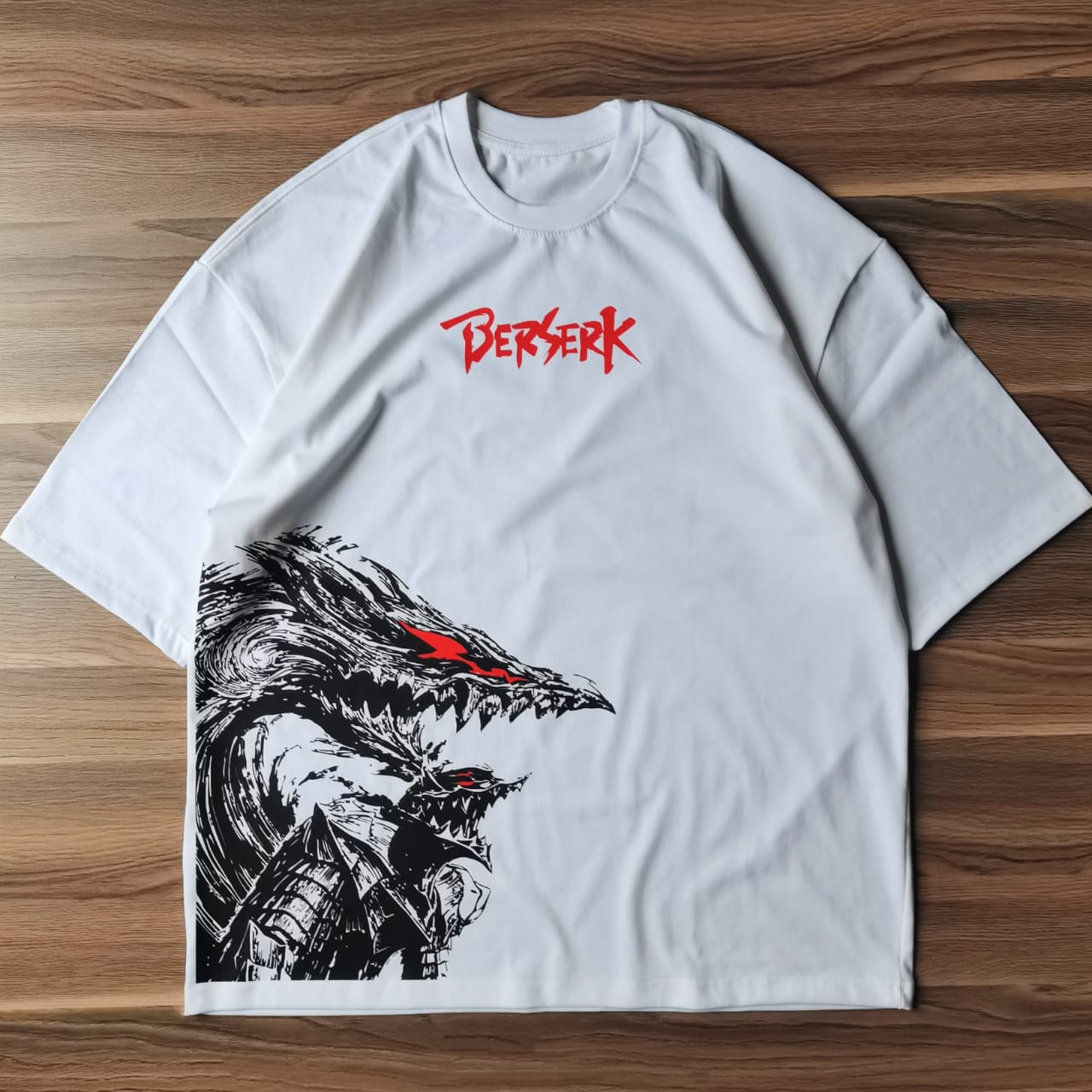 تيشيرت أبيض أوفرسايز عليه تصميم لشخصية جاتس من أنمي بيرزيرك بداخل البيرزيركر آرمور باللون الأسود مع تفاصيل حمراء من متصور من فوق وخلفية خشبية مقدم من Sugoi Store